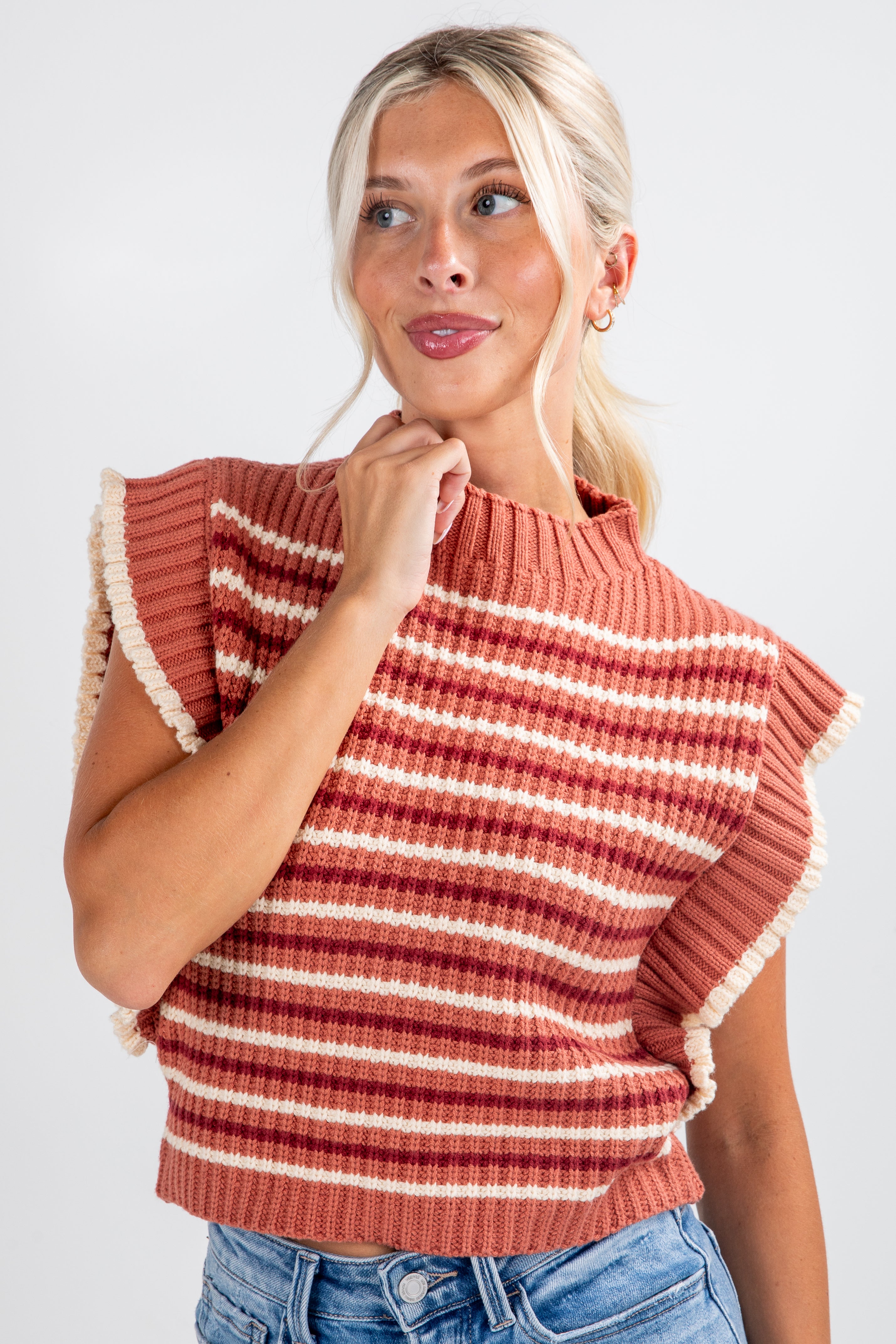 Woman wearing a rust-colored striped sweater with ruffled shoulders against a white background