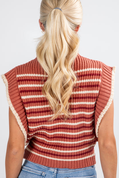 Person wearing a striped sleeveless sweater with ruffled edges on a plain background