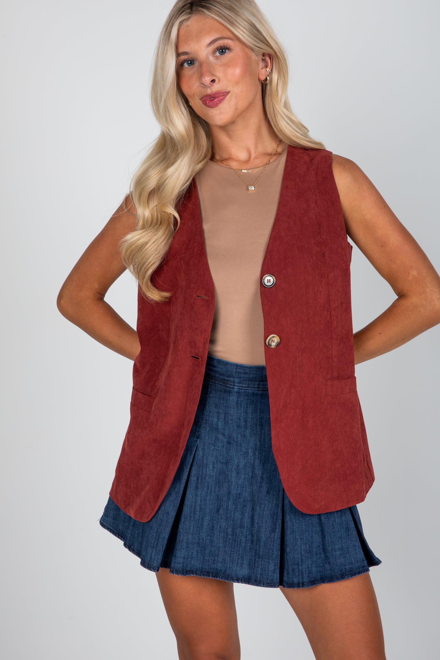 Woman wearing a red vest over a beige top and blue skirt on a plain background