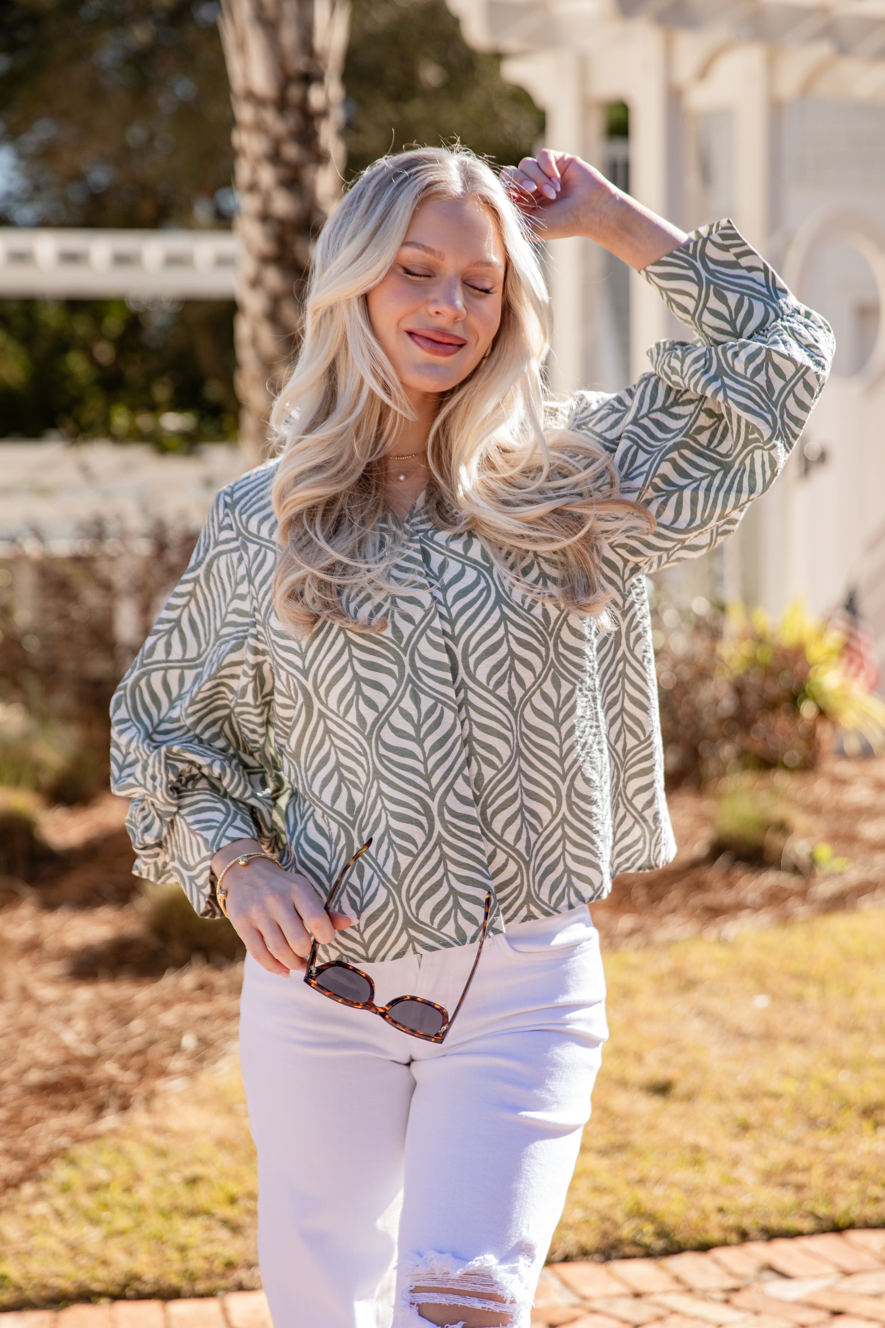 Woman wearing a patterned blouse and white pants outdoors