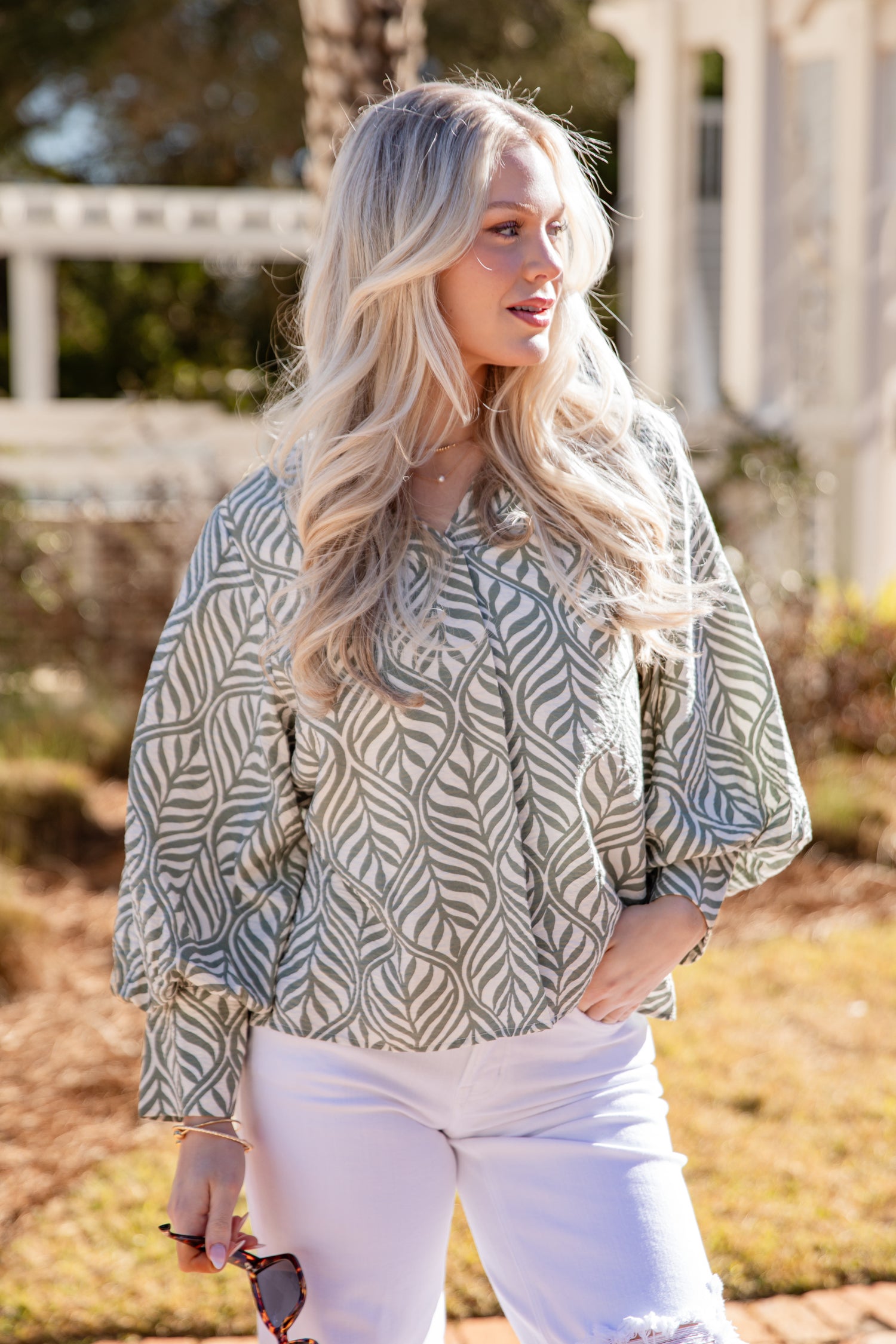 Woman wearing a patterned blouse and white pants outdoors