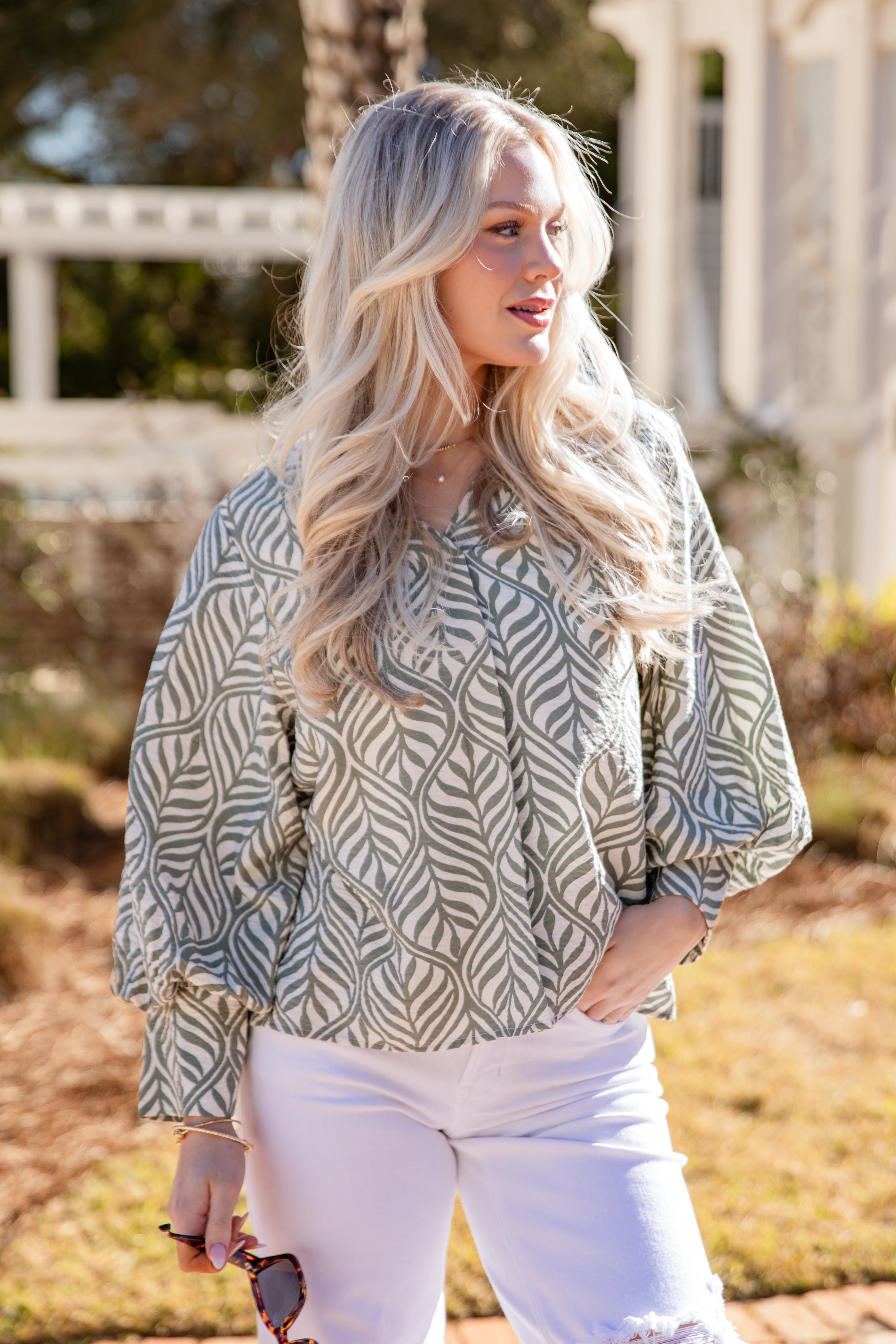 Woman wearing a patterned blouse and white pants outdoors
