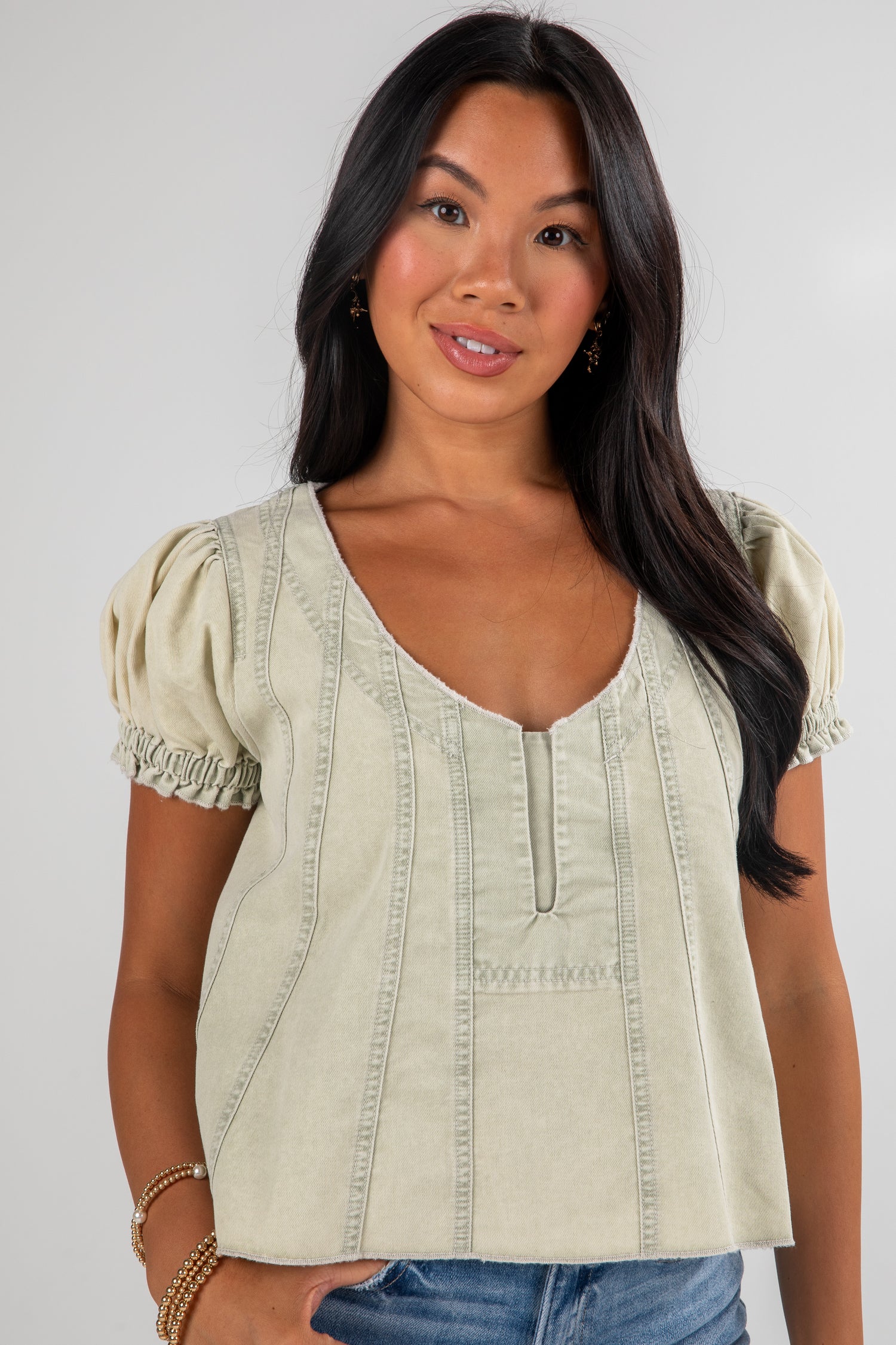 Woman wearing a light-colored blouse with short sleeves against a plain background