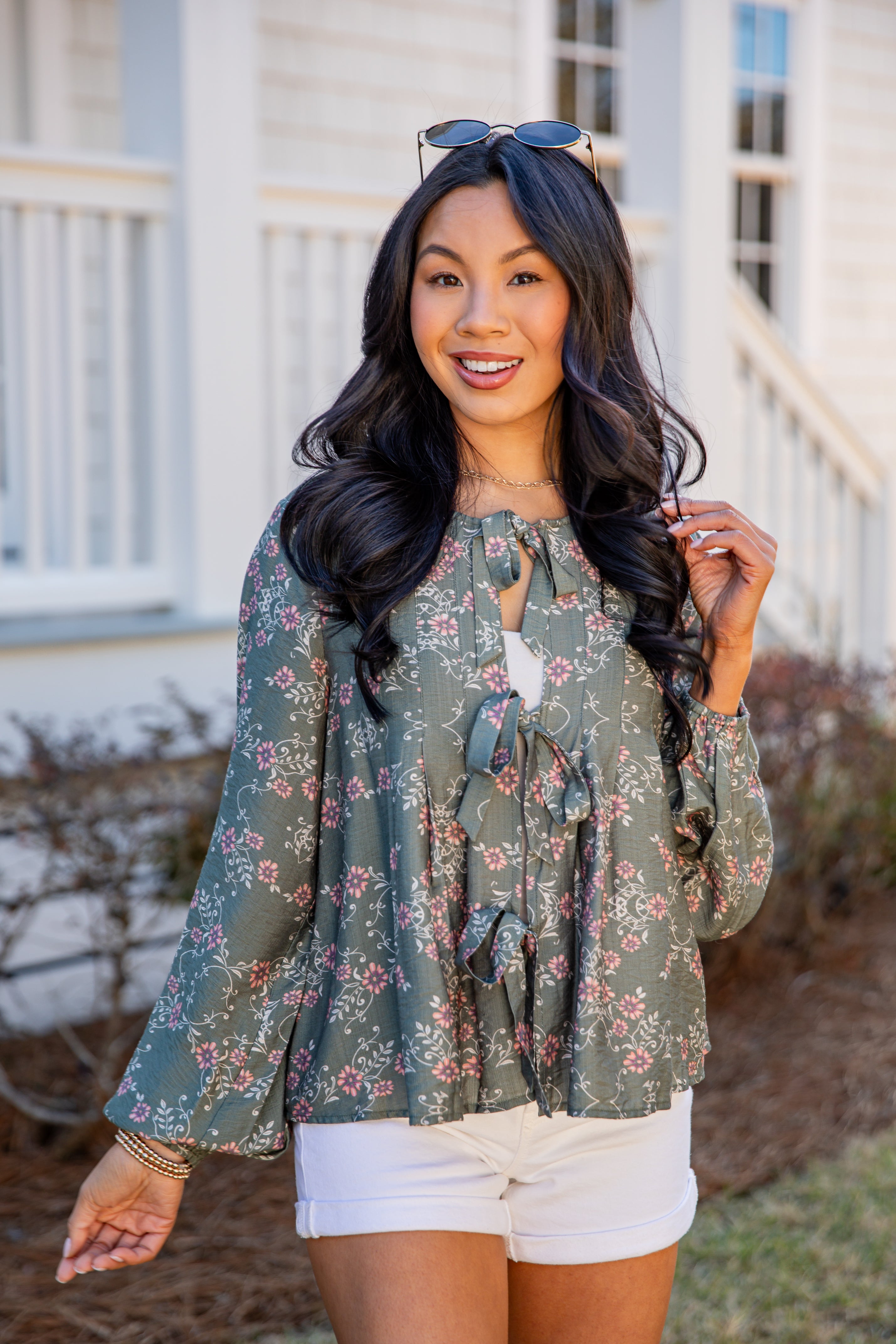 Woman wearing a floral blouse and white shorts outdoors.