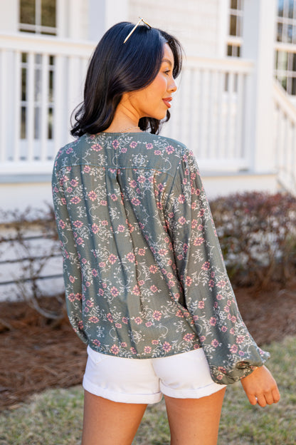 Woman wearing a floral blouse and white shorts standing outdoors.