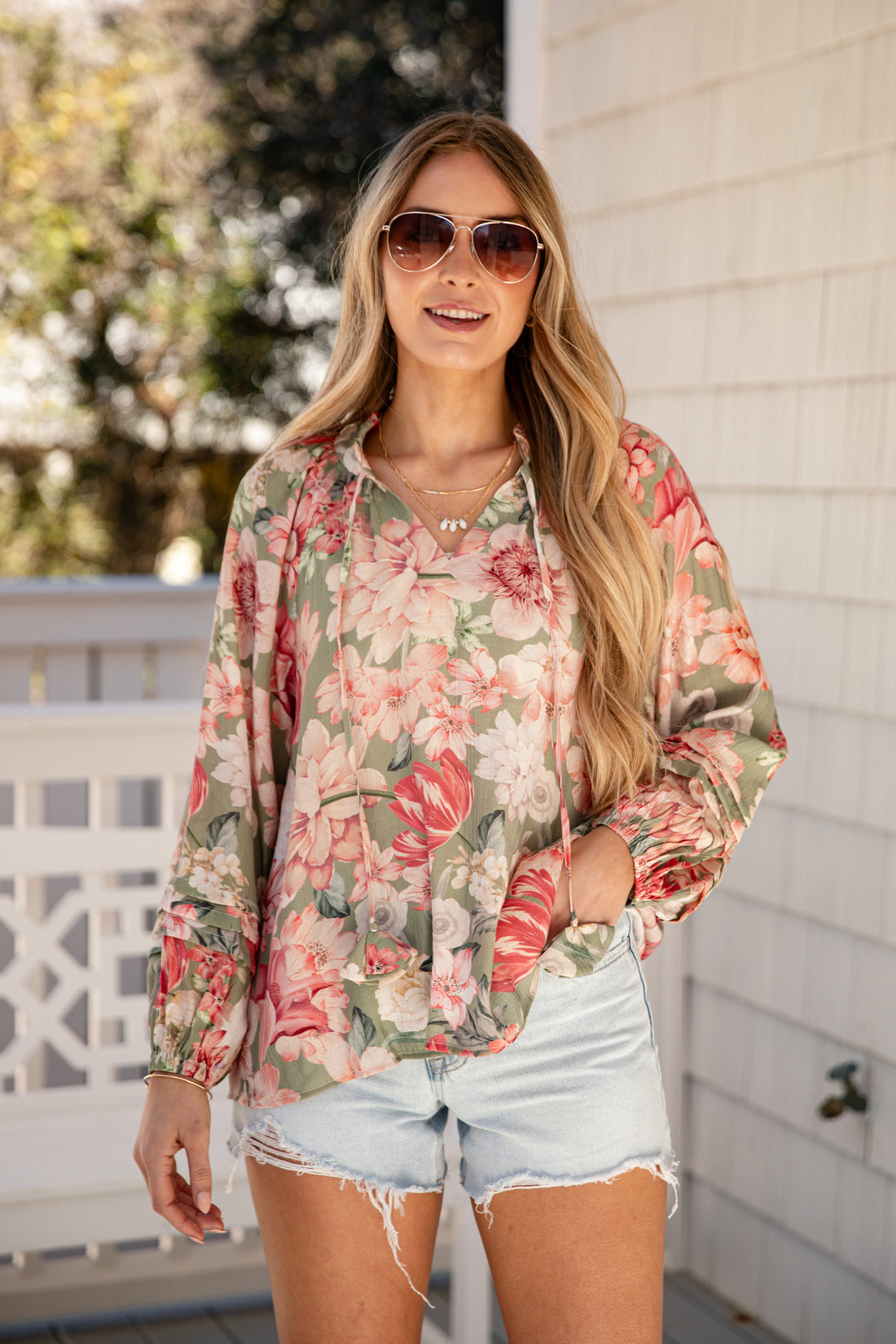 Woman wearing a floral blouse and denim shorts outdoors.