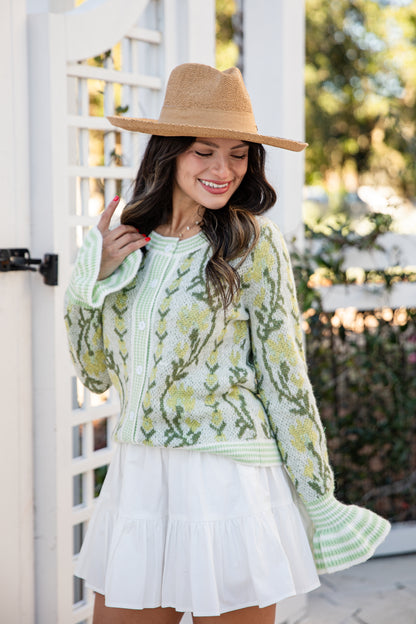 Woman wearing a green floral dress and beige hat outdoors