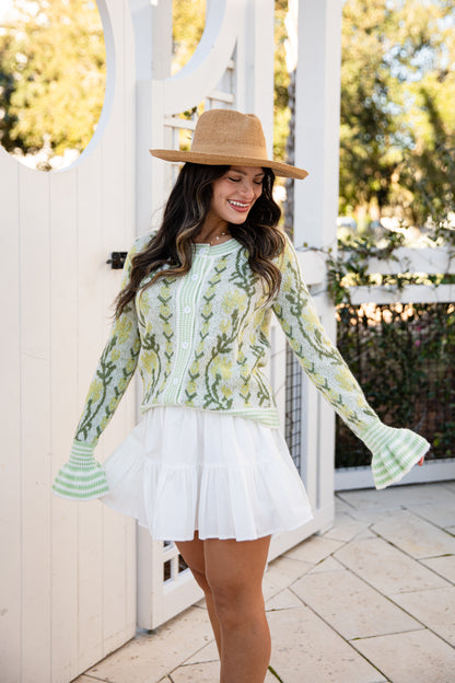 Woman wearing a floral blouse and white skirt with a straw hat outdoors.