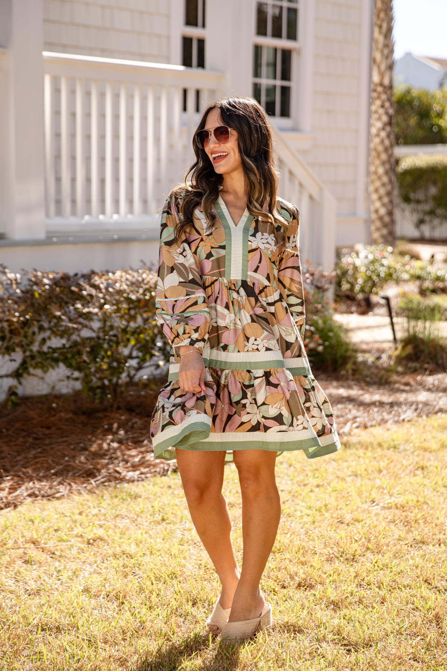 Woman in a patterned dress standing outdoors with a house in the background