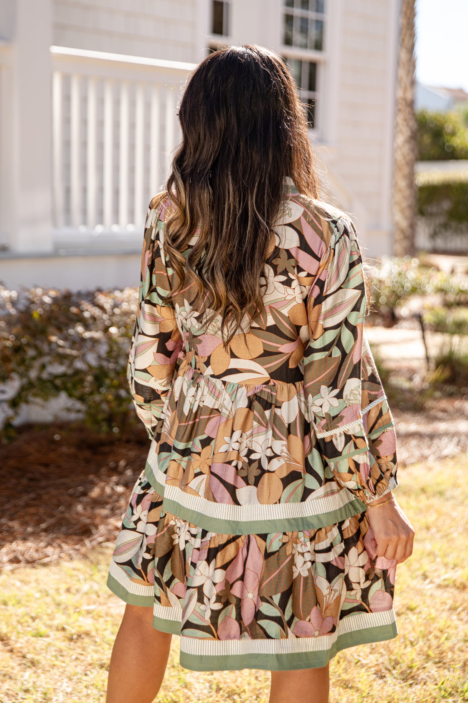 Woman wearing a floral dress standing outdoors with a house and garden in the background