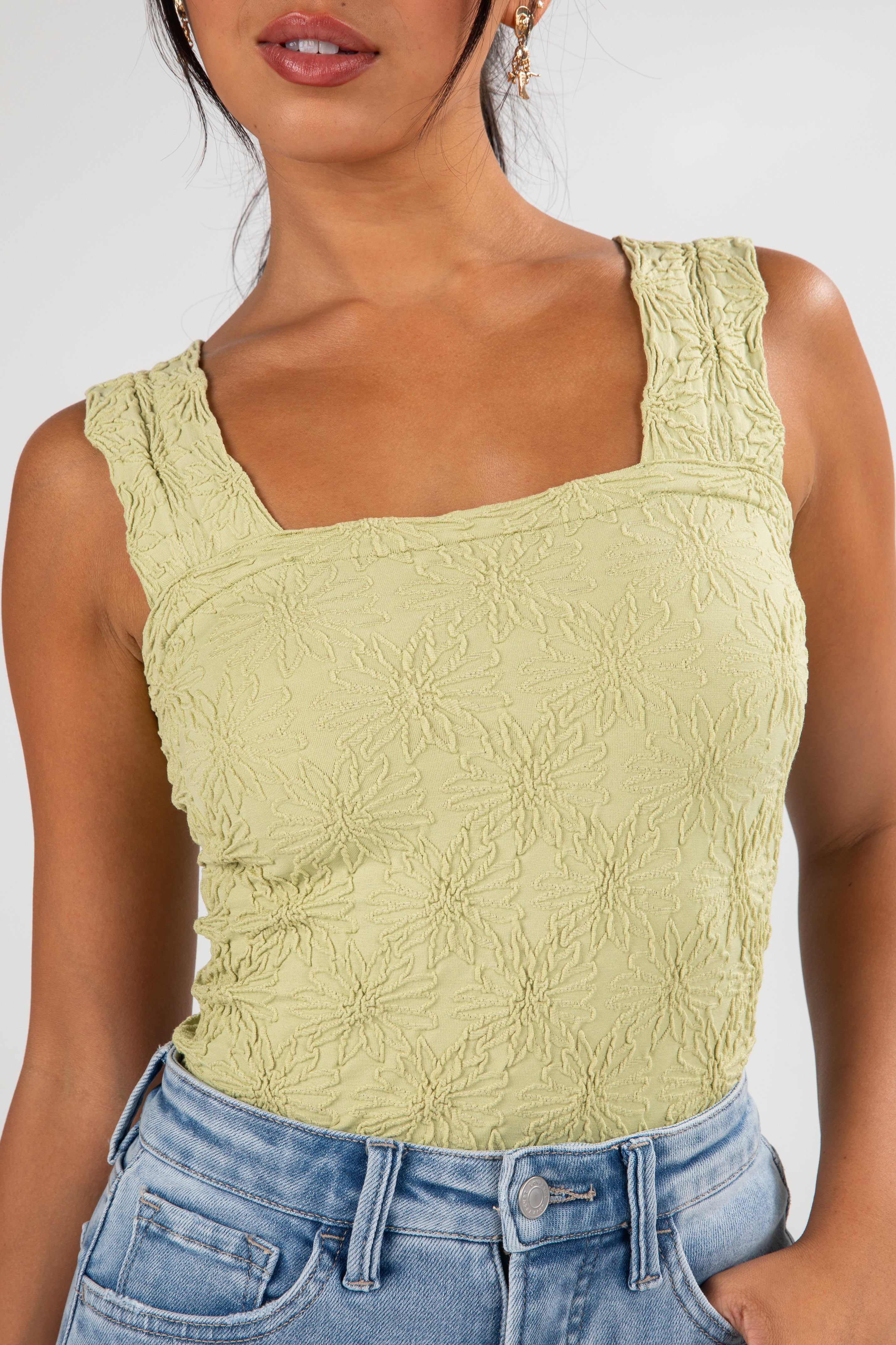 Woman wearing a light green textured tank top and blue jeans against a white background