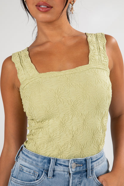 Woman wearing a light green textured tank top and blue jeans against a white background