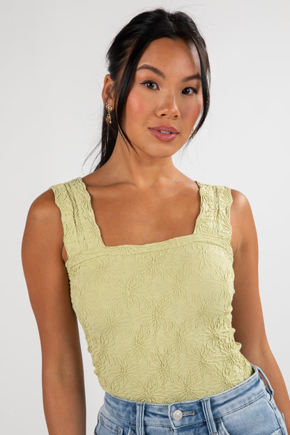 Woman wearing a light green sleeveless top against a white background