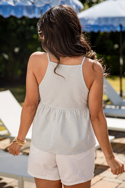Woman wearing a light-colored sleeveless top and white shorts standing on a sunlit deck with umbrellas in the background.