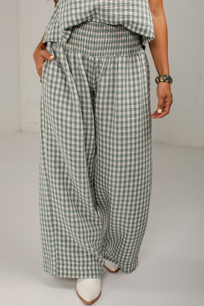A person wearing wide-leg cropped pants in a green and white gingham check pattern, paired with a matching green and white gingham top and white pointed-toe heels, photographed against a plain light gray studio background.
