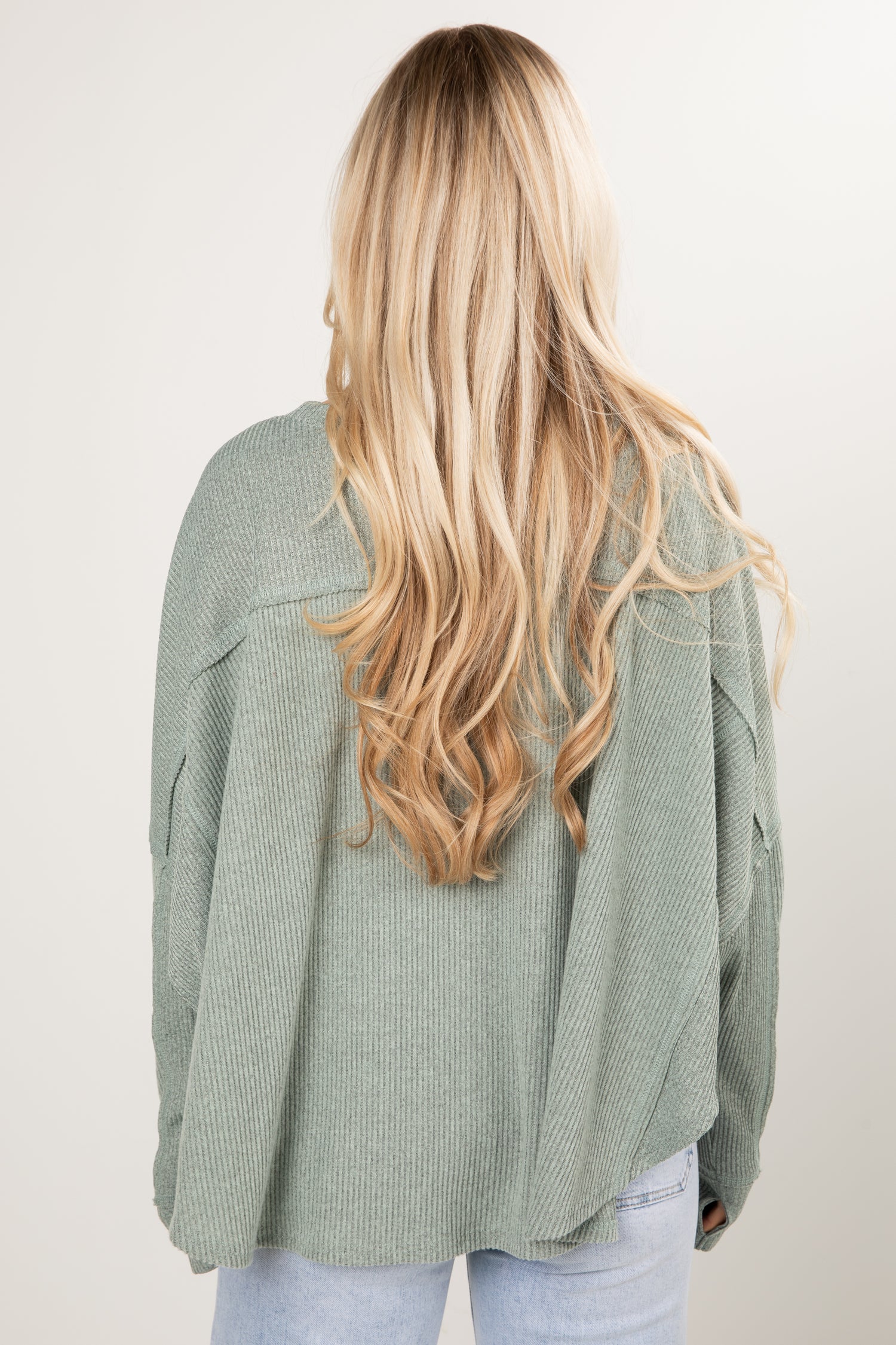 Woman wearing a sage green sweater and blue jeans on a white background