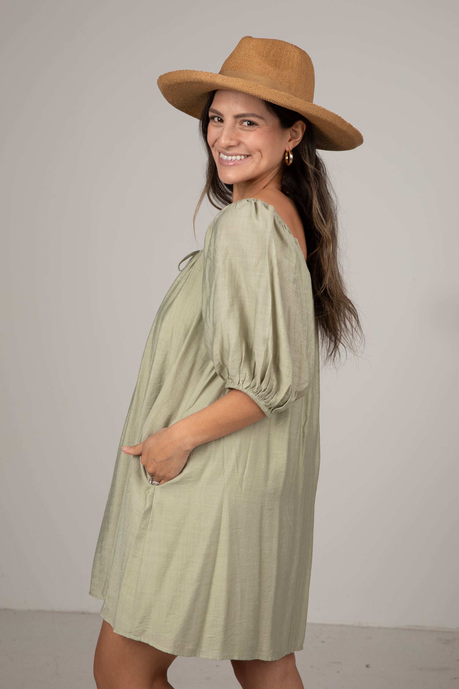 Woman wearing a green dress and brown hat against a plain background