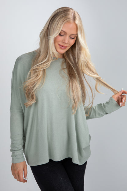 Woman wearing a light green long-sleeve top against a gray background