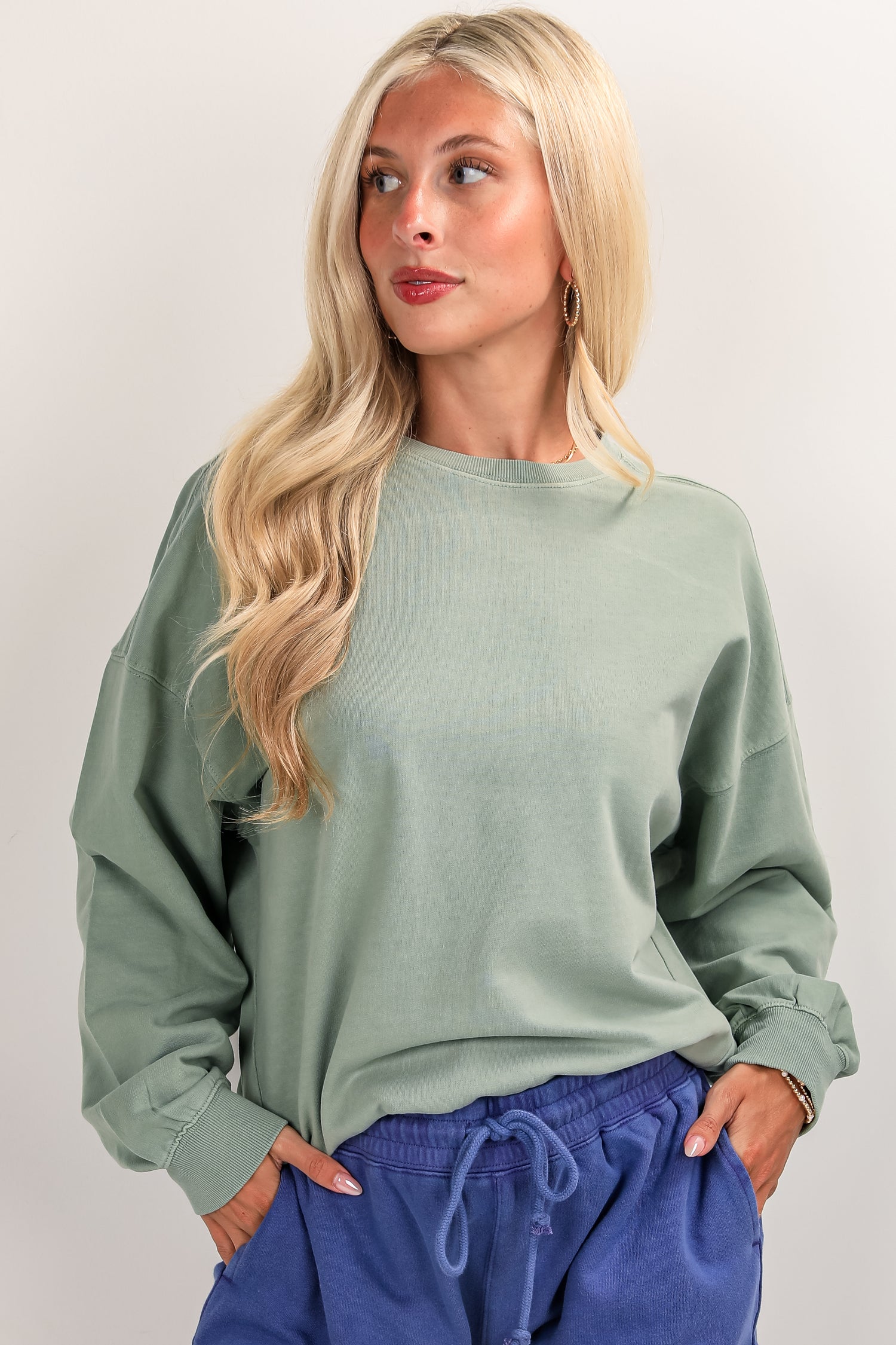 Woman wearing a green sweatshirt and blue pants against a plain background