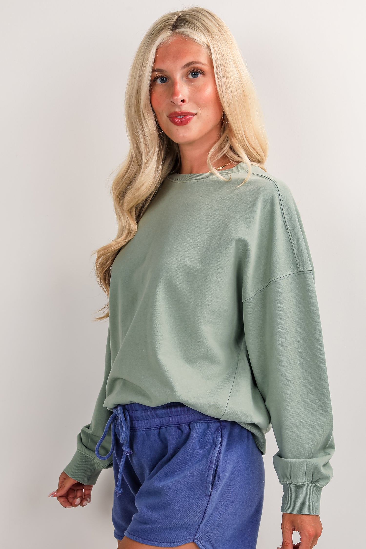 Woman wearing a green sweatshirt and blue shorts on a white background