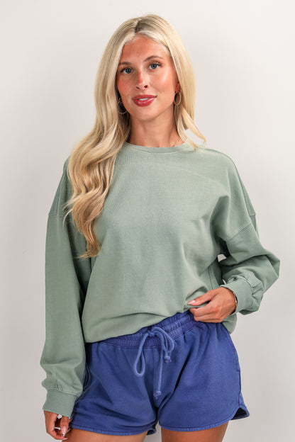 Woman wearing a green sweatshirt and blue shorts against a plain background