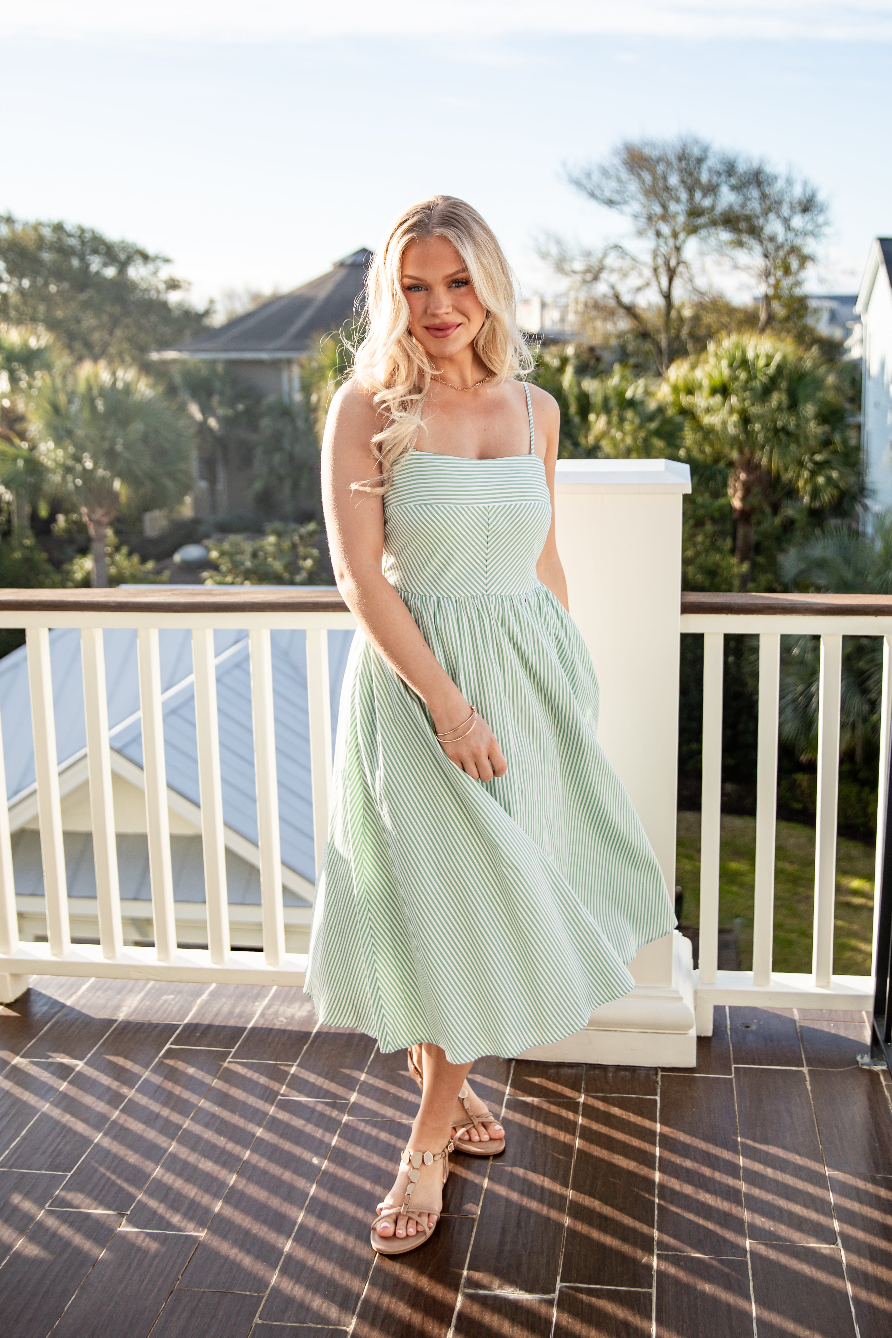 Woman in a light green dress standing on a balcony with trees in the background