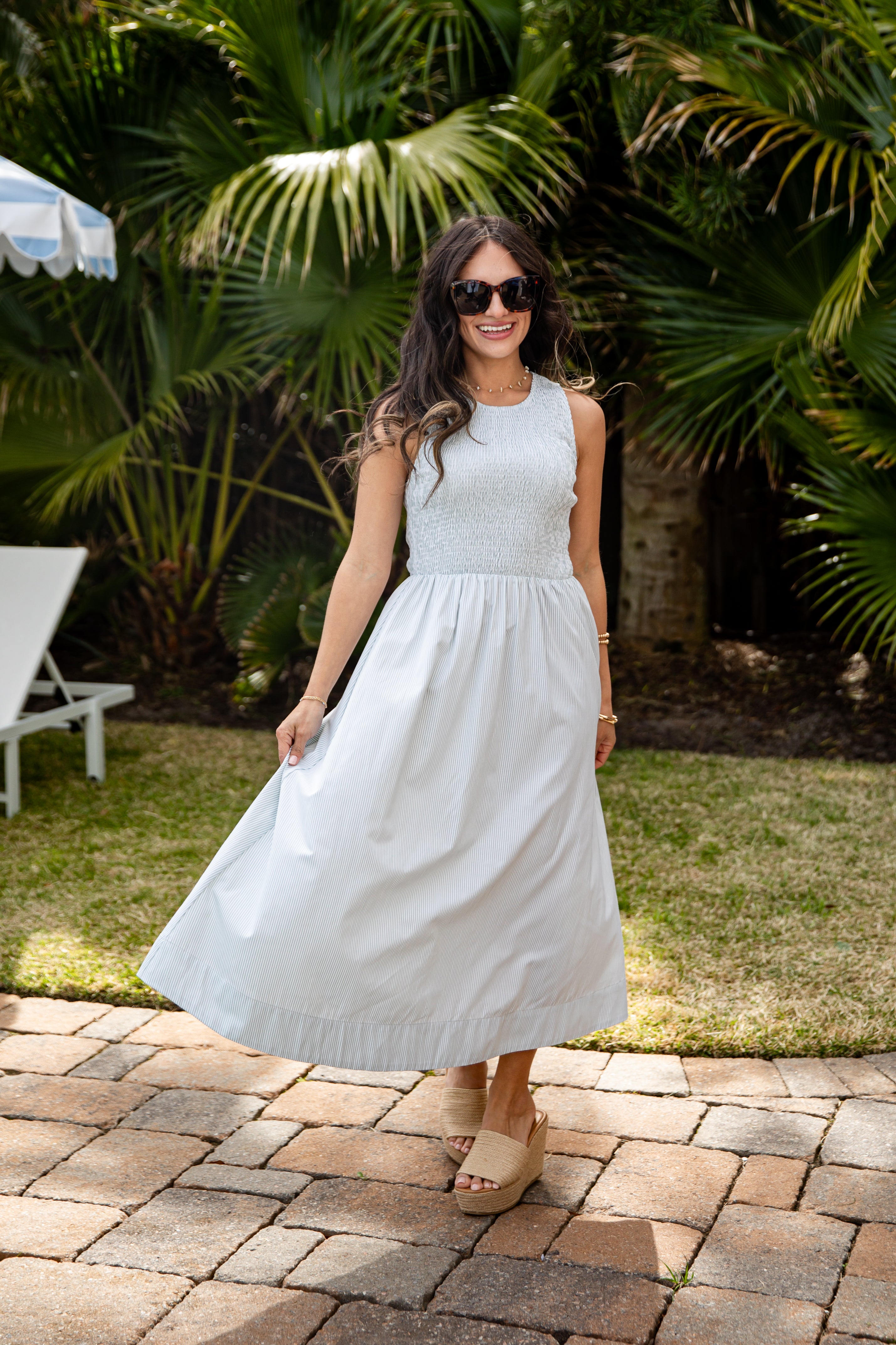 Woman in a light blue dress standing on a patio with greenery in the background