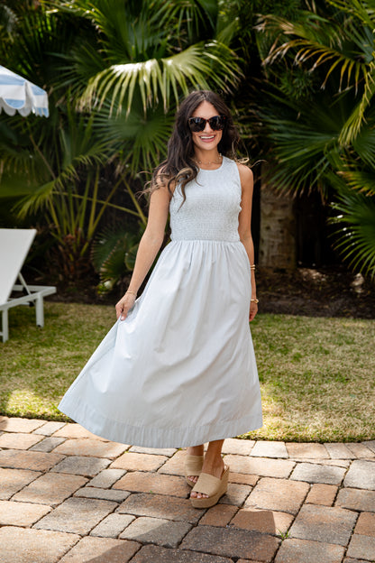 Woman in a light blue dress standing on a patio with greenery in the background