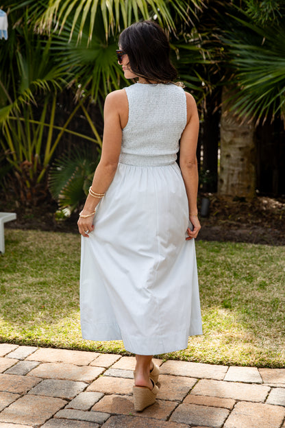 Woman in a light gray dress standing outdoors with greenery in the background