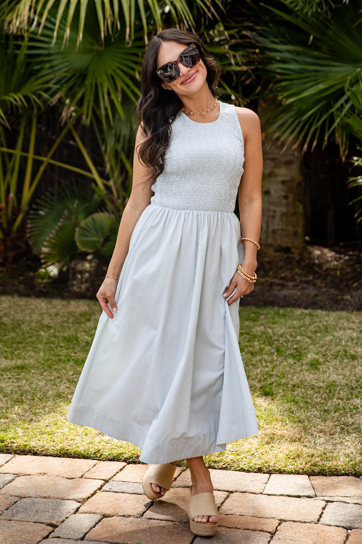 Woman in a light blue dress standing outdoors with greenery in the background