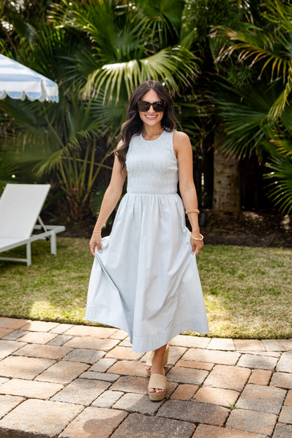 Woman in a light blue dress standing outdoors with greenery in the background