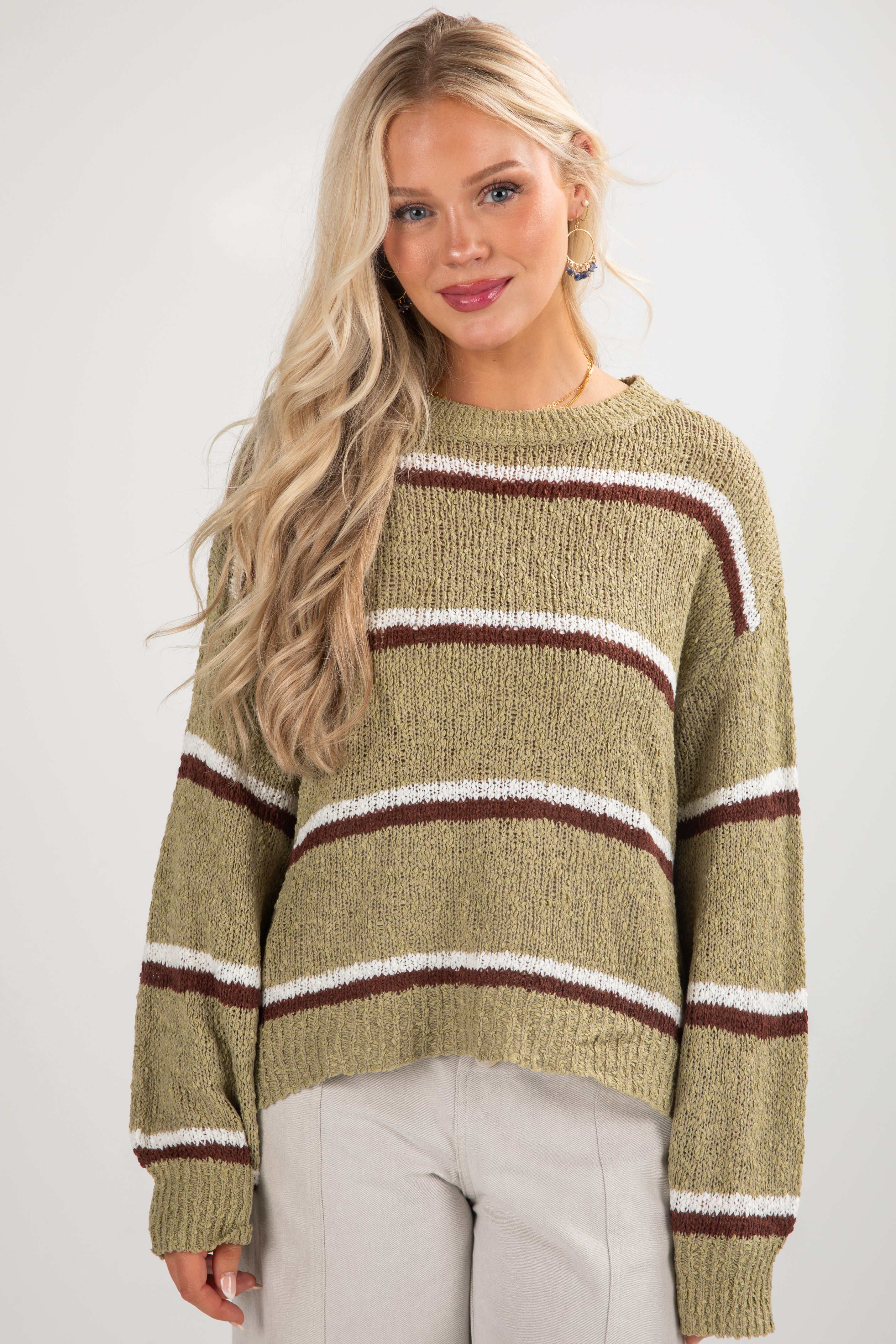 Woman wearing a green sweater with brown and white stripes on a white background