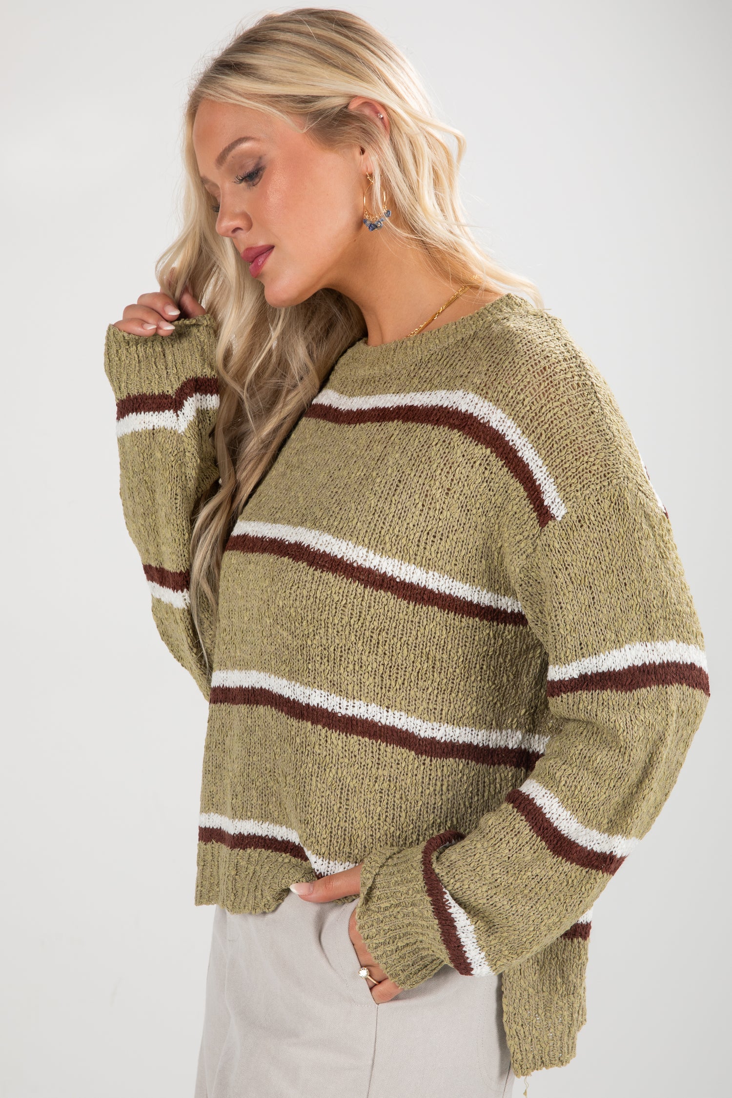 Woman wearing a green sweater with brown and white stripes on a white background