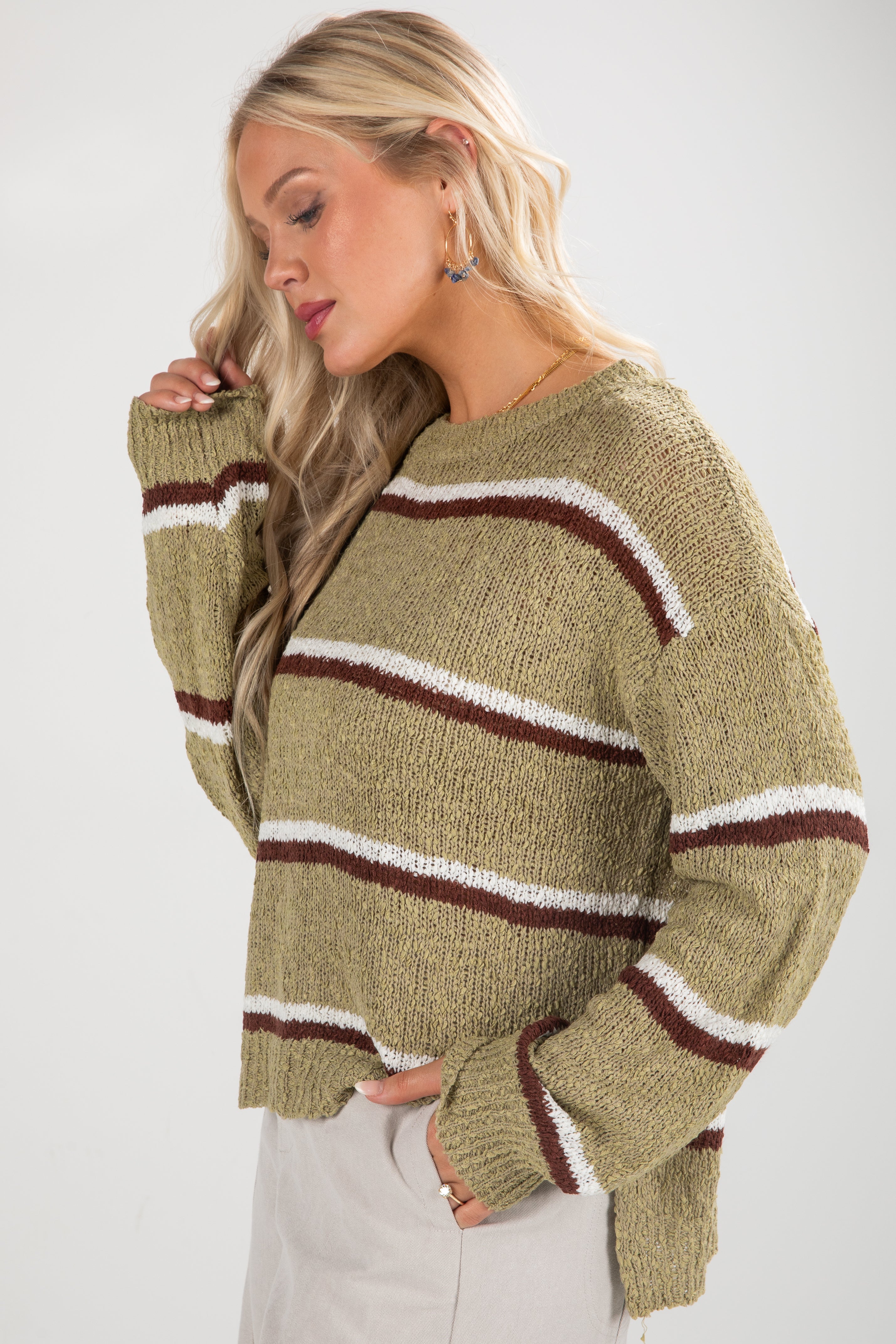 Woman wearing a green sweater with brown and white stripes on a white background