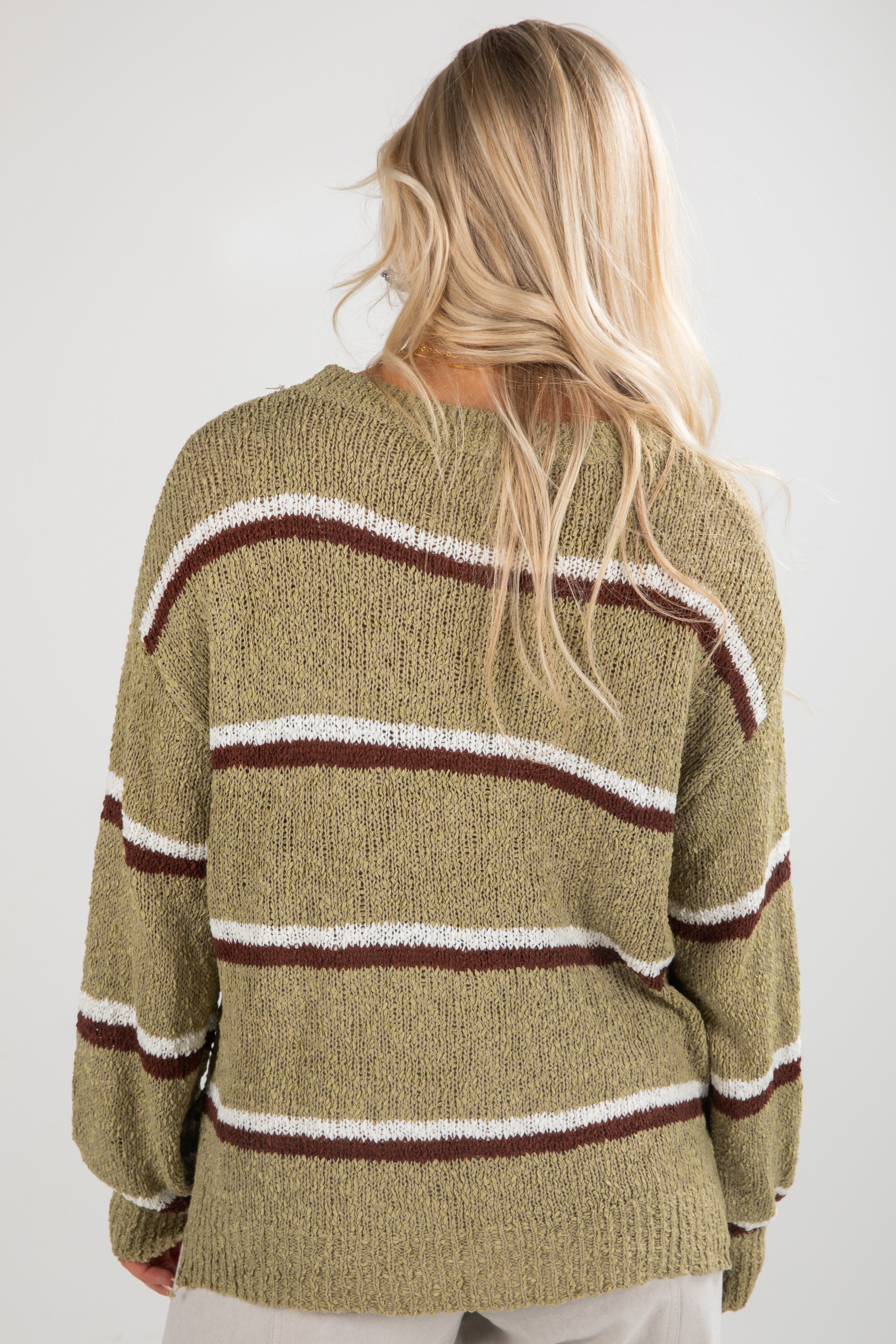 Person wearing a green sweater with brown and white stripes on a plain background