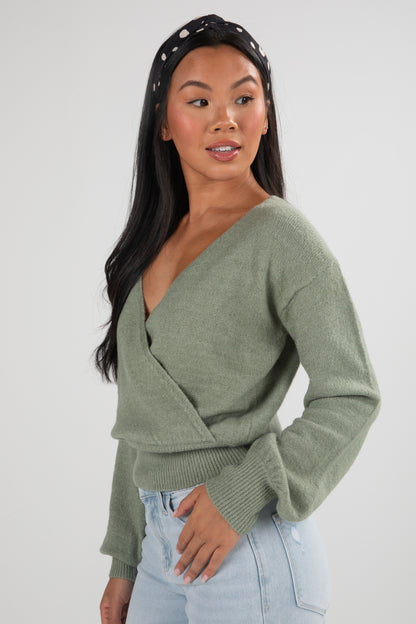 Woman wearing a green sweater and light blue jeans against a white background