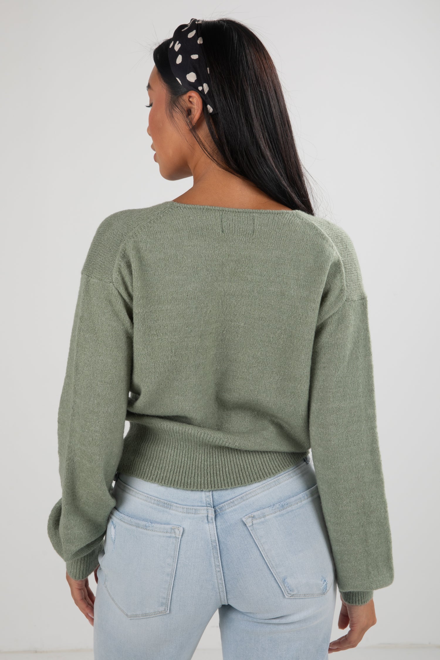 Person wearing a green sweater and light blue jeans with a white background