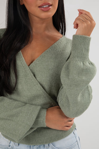 Woman wearing a green sweater with balloon sleeves against a white background