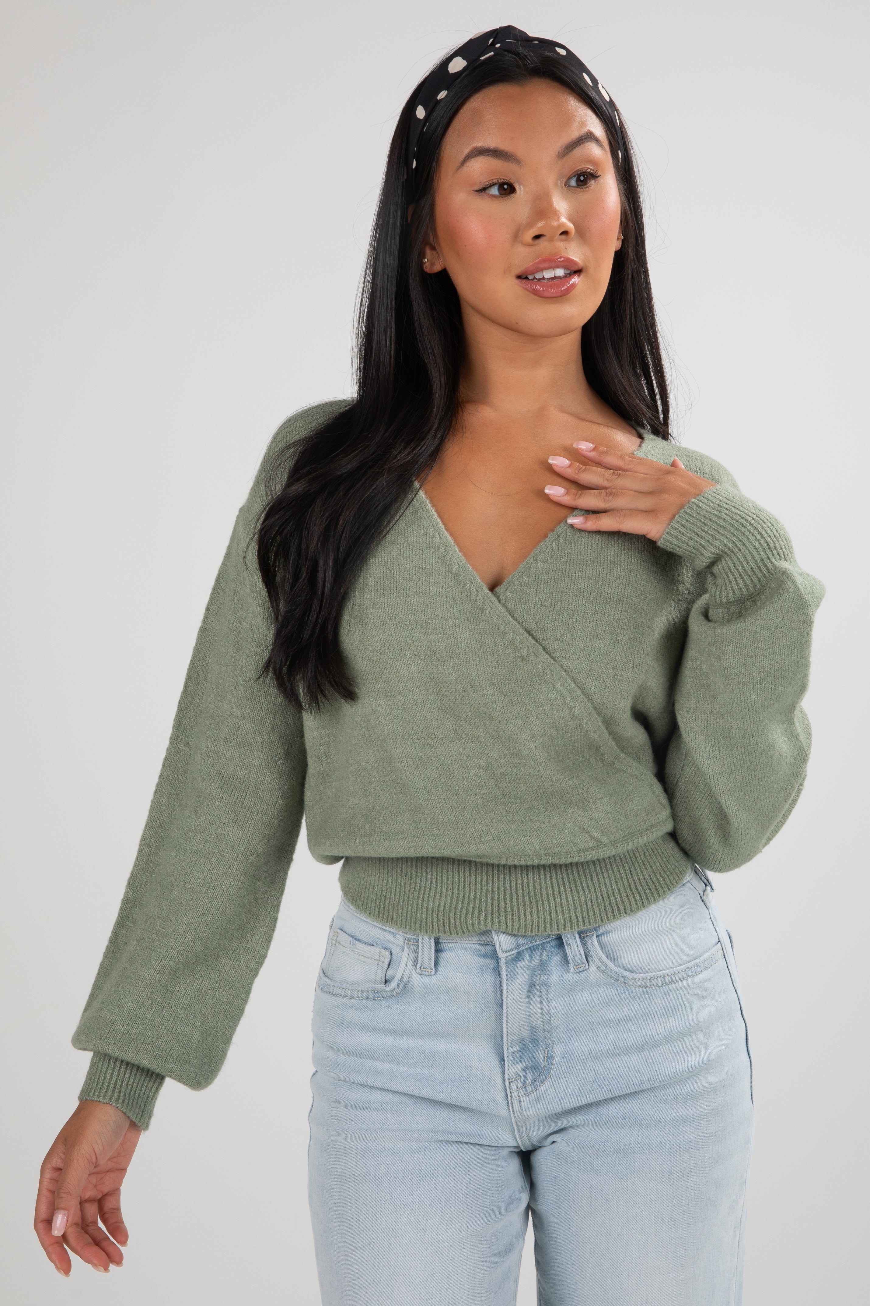 Woman wearing a green sweater and light blue jeans on a white background