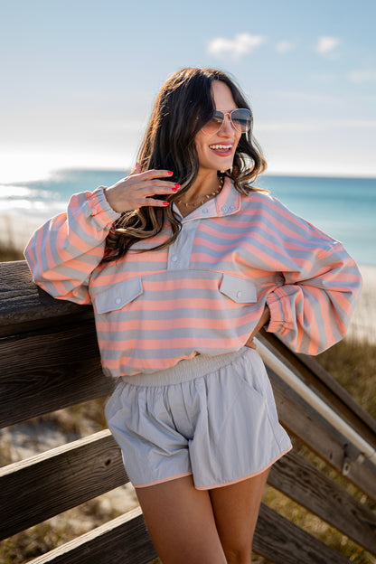 Woman wearing a striped shirt and shorts standing by a wooden railing with an ocean view.