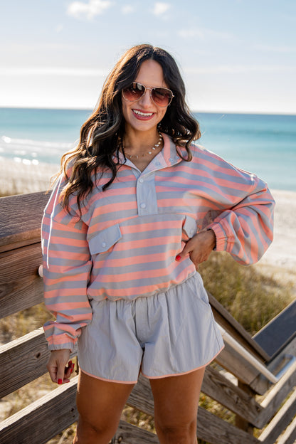 Woman wearing a striped shirt and shorts standing on a wooden deck by the beach.