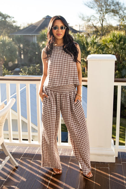 Woman in a checkered outfit standing on a balcony with trees and a house in the background.