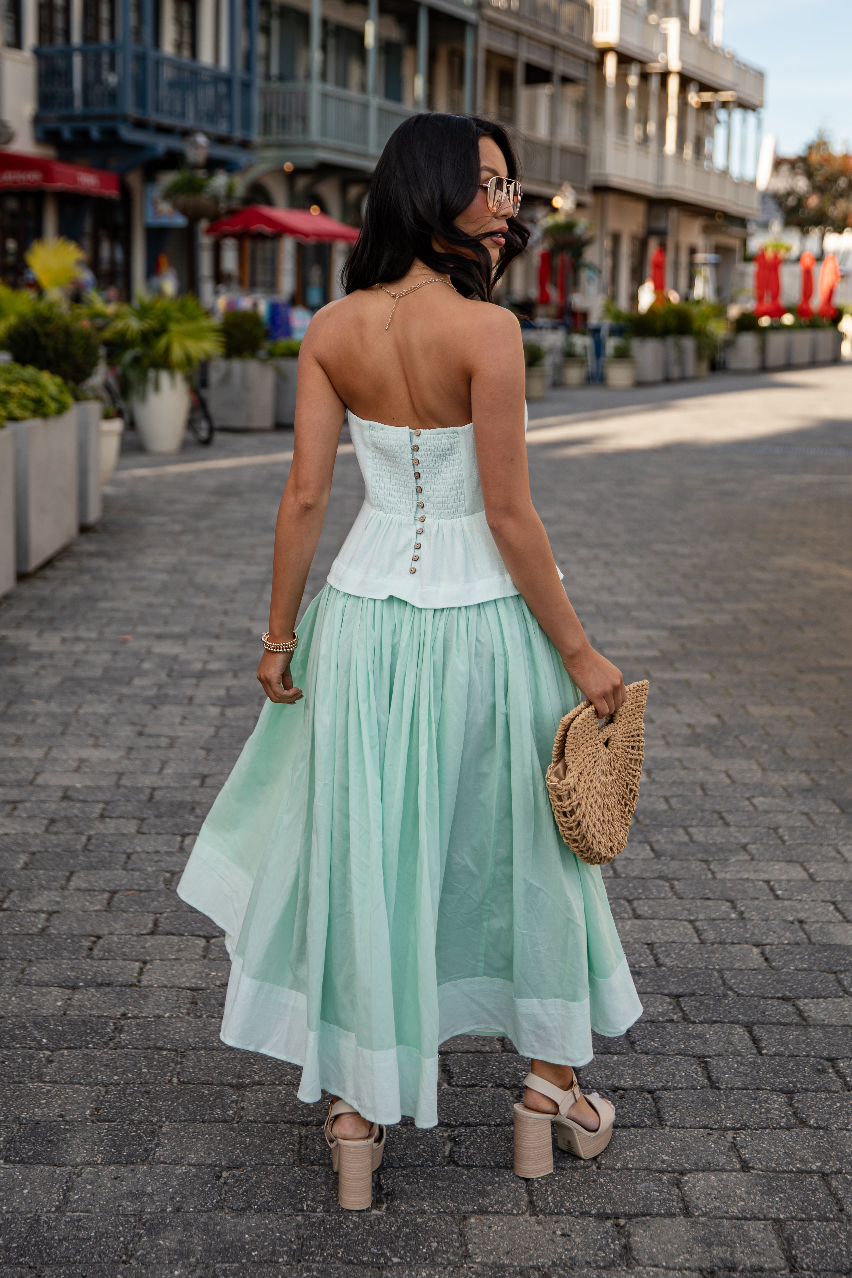 Woman in a light green dress walking on a street with shops in the background