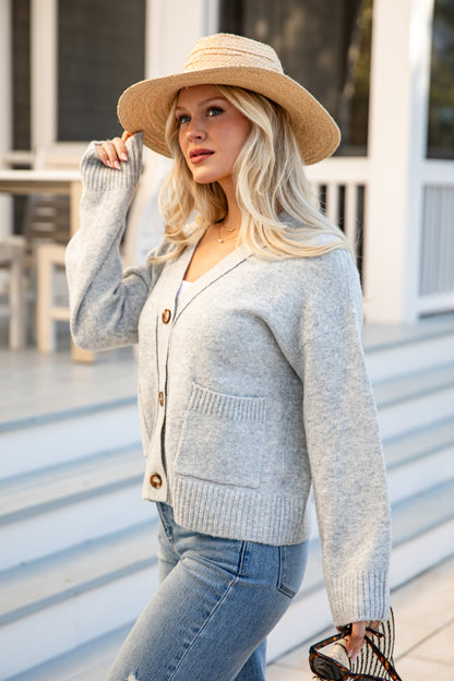 Woman wearing a light gray cardigan, beige hat, and blue jeans outdoors.