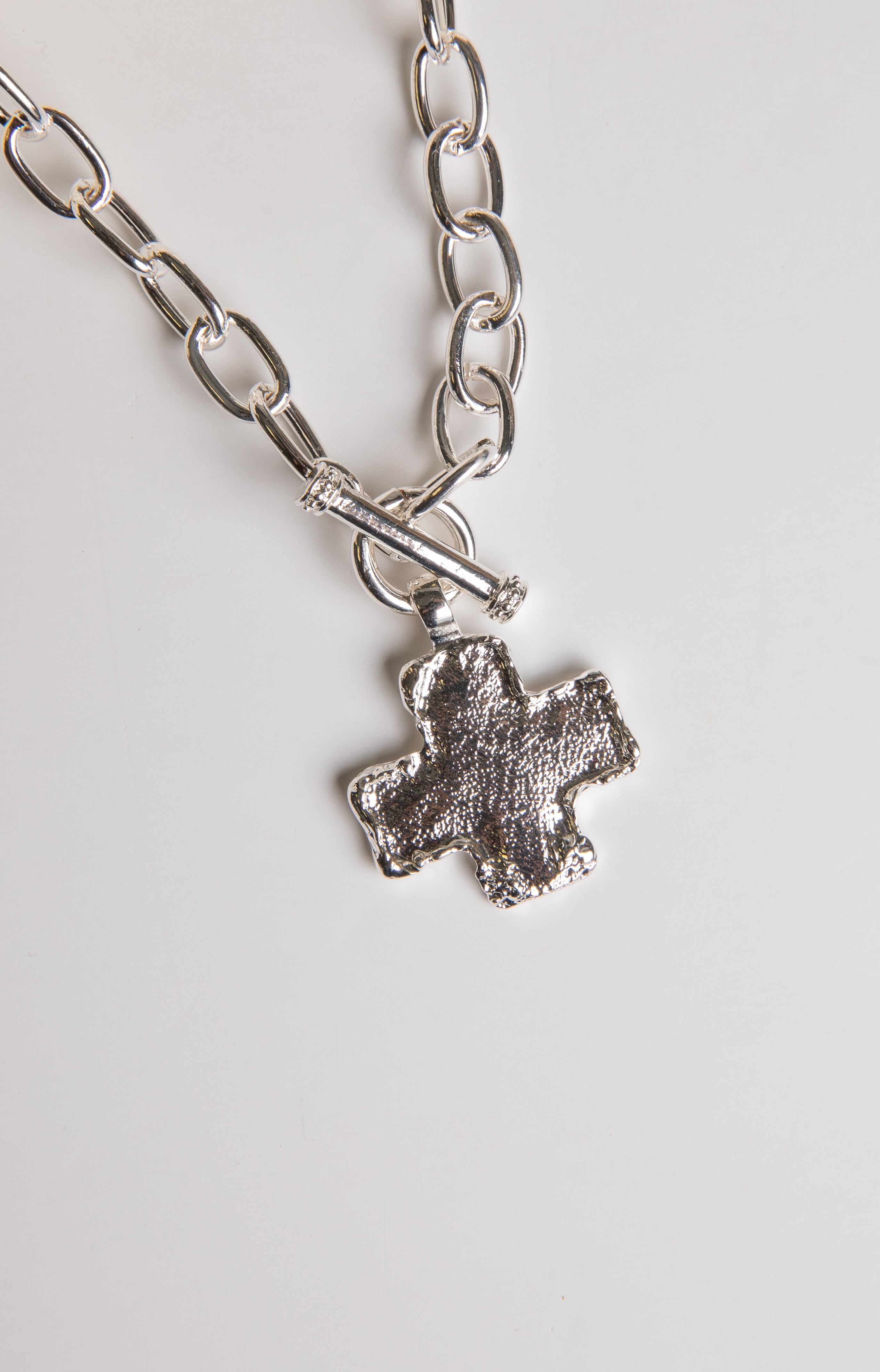 Silver chain necklace with a cross pendant on a light gray background