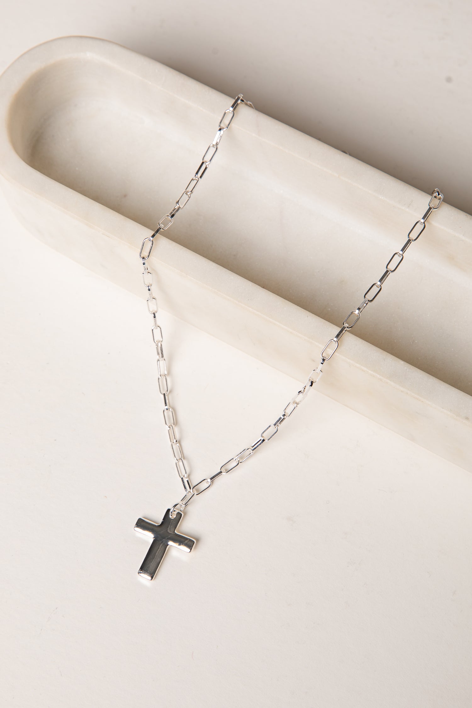 Silver necklace with a cross pendant on a white surface