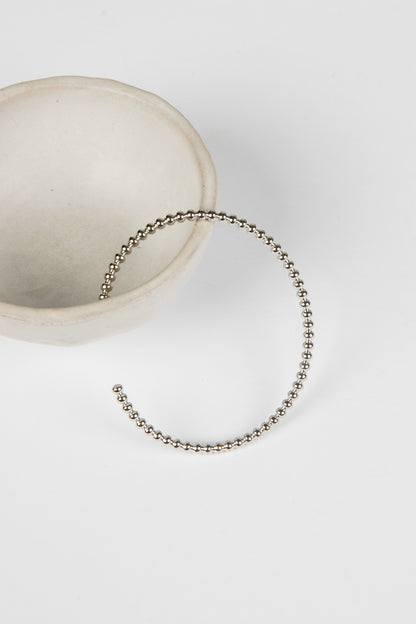 Silver beaded bracelet on a white surface with a neutral background
