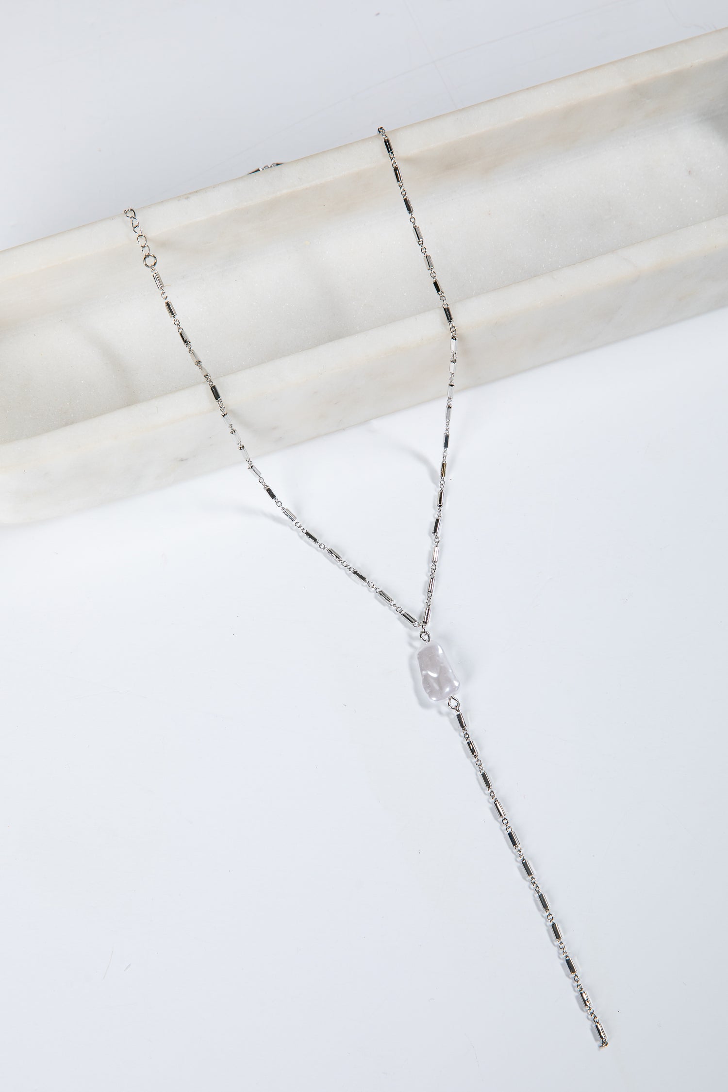 Silver necklace with a clear pendant on a marble surface