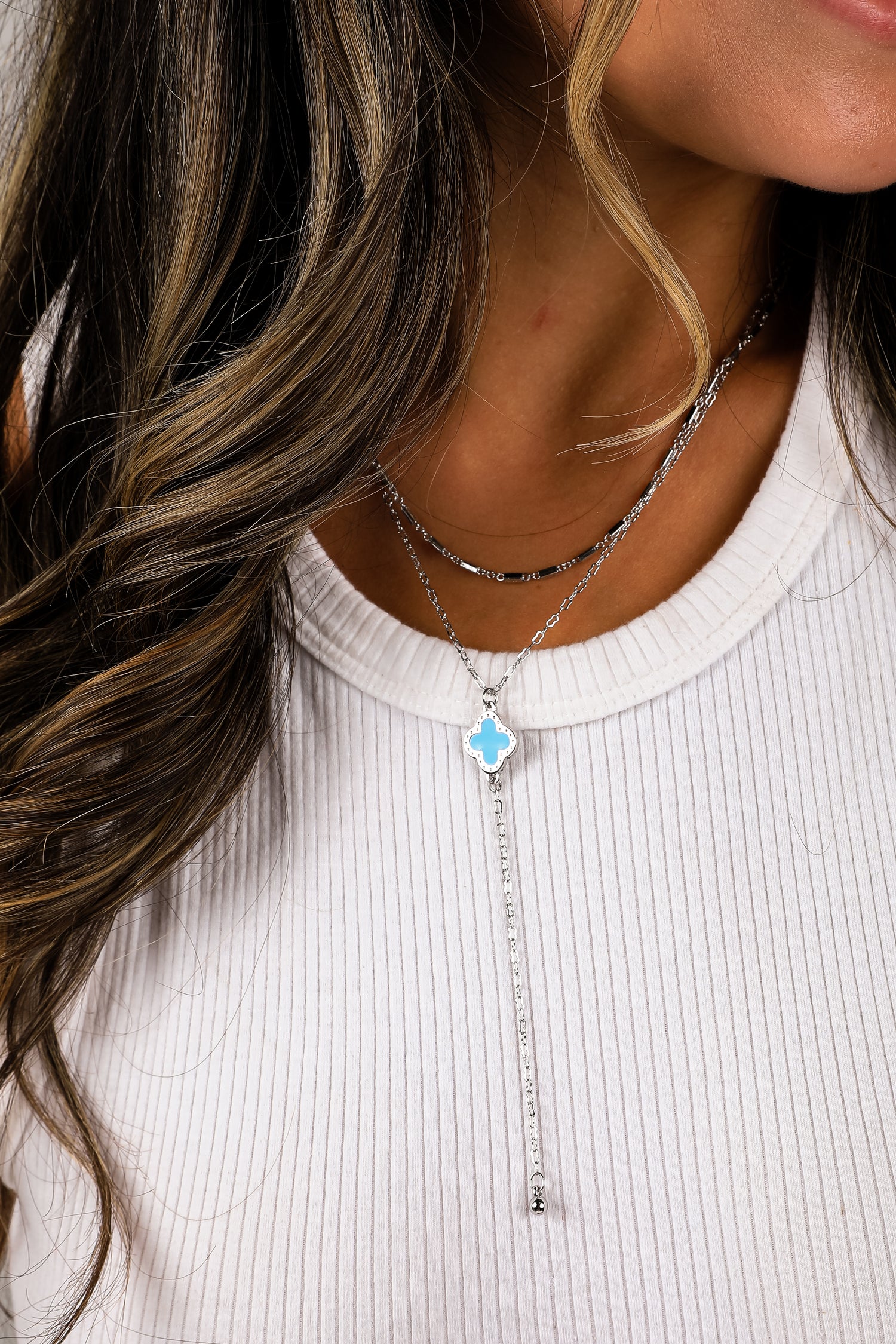 Close-up of a woman wearing a silver necklace with a blue pendant on a white background