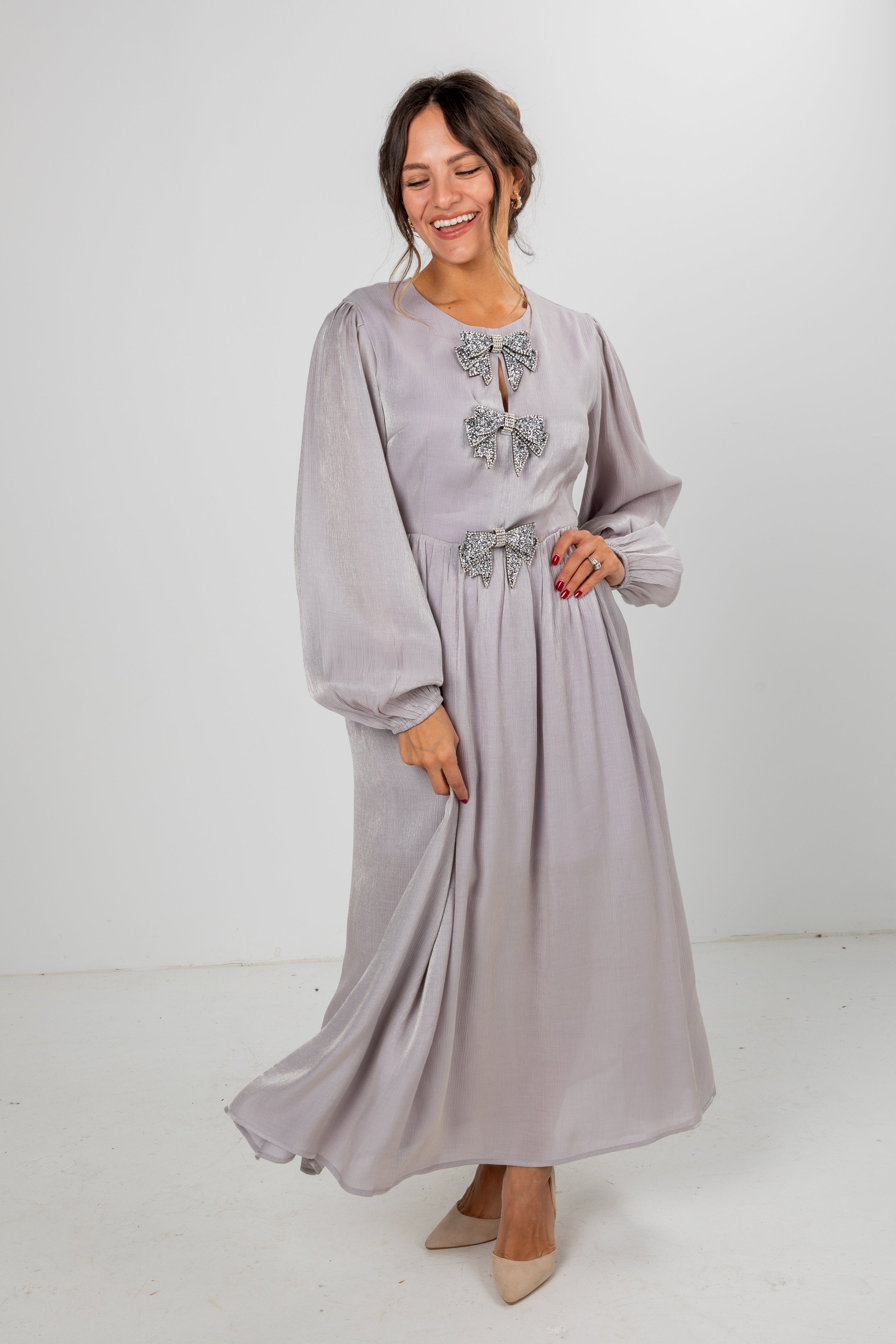 Woman wearing a long, light gray dress with decorative bows on a white background
